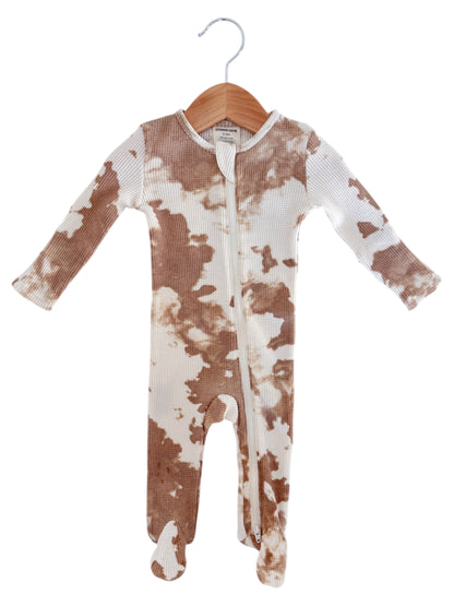 Brown and white patterned baby onesie hanging on a wooden hanger.