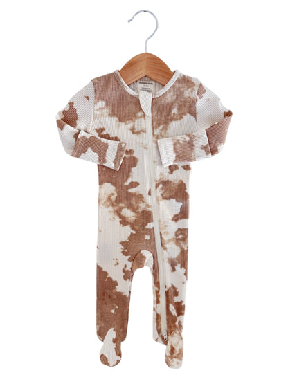 Tan and white baby onesie with long sleeves and feet, displayed on a wooden hanger.