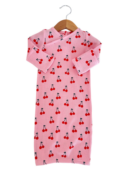 Pink children's dress with cherry print, featuring long sleeves and a hanging loop. Suitable for casual wear.