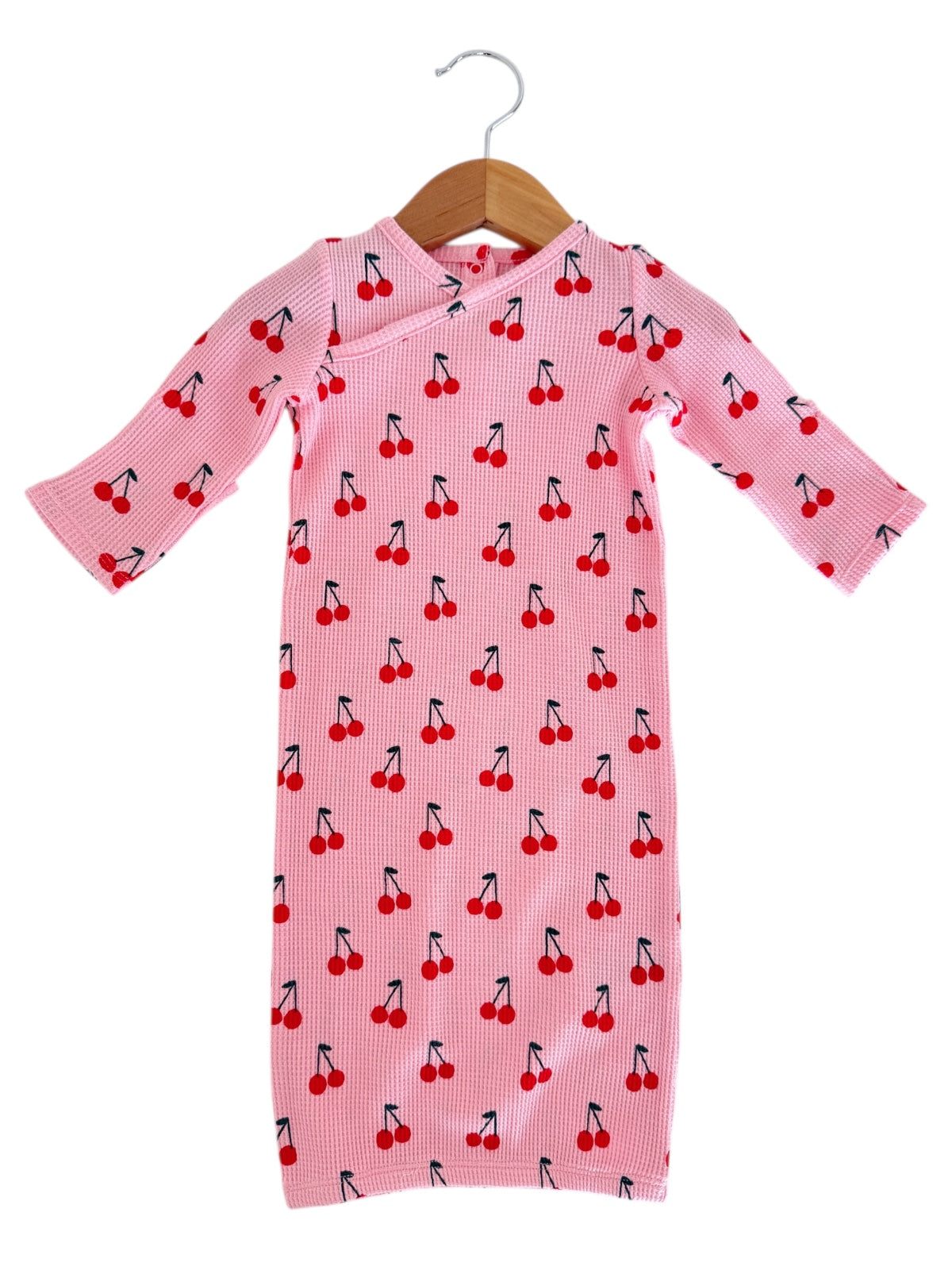 Pink dress with red cherry print, hanging on a wooden hanger.