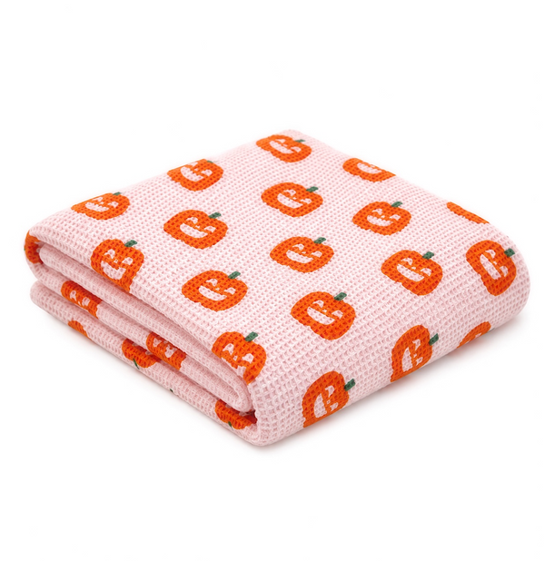 Folded kitchen towel featuring a pink background with orange pumpkin patterns. Perfect for seasonal decor.