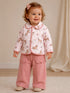 Toddler in a pink horse-patterned jacket and pink pants, smiling with a bow in her hair.