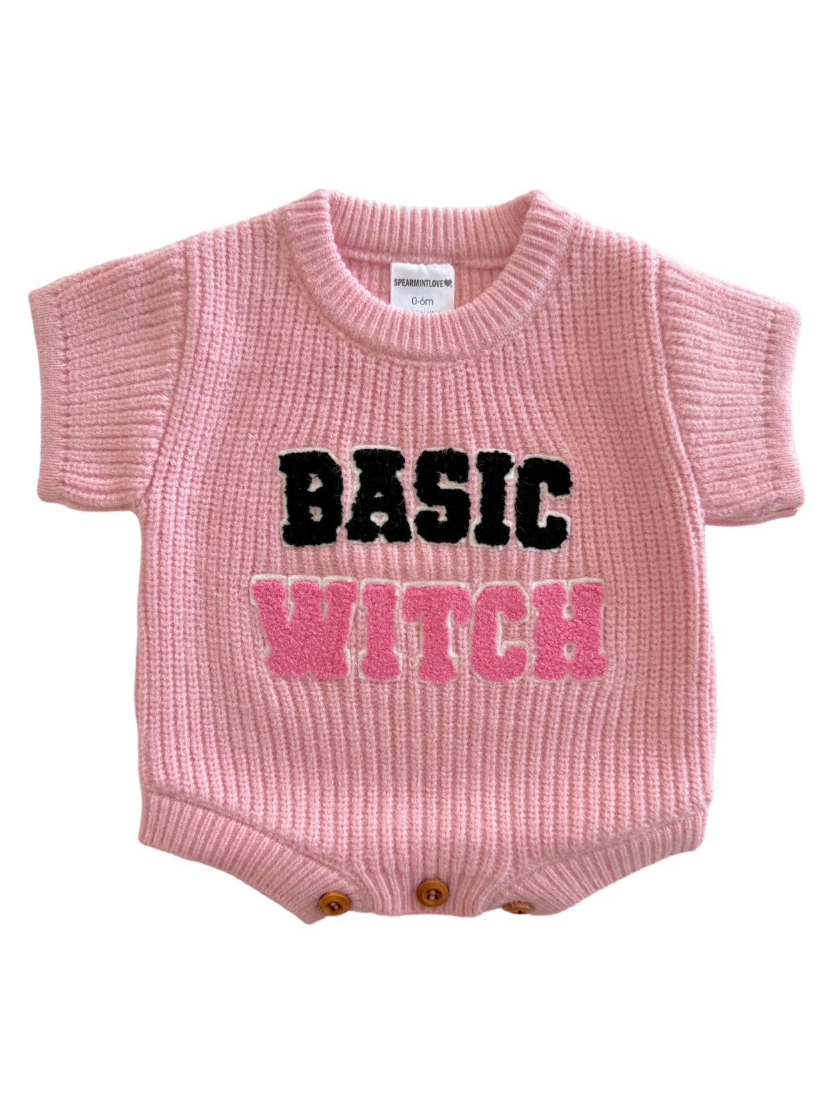 Pink knitted baby onesie with "BASIC WITCH" in bold, colorful letters.