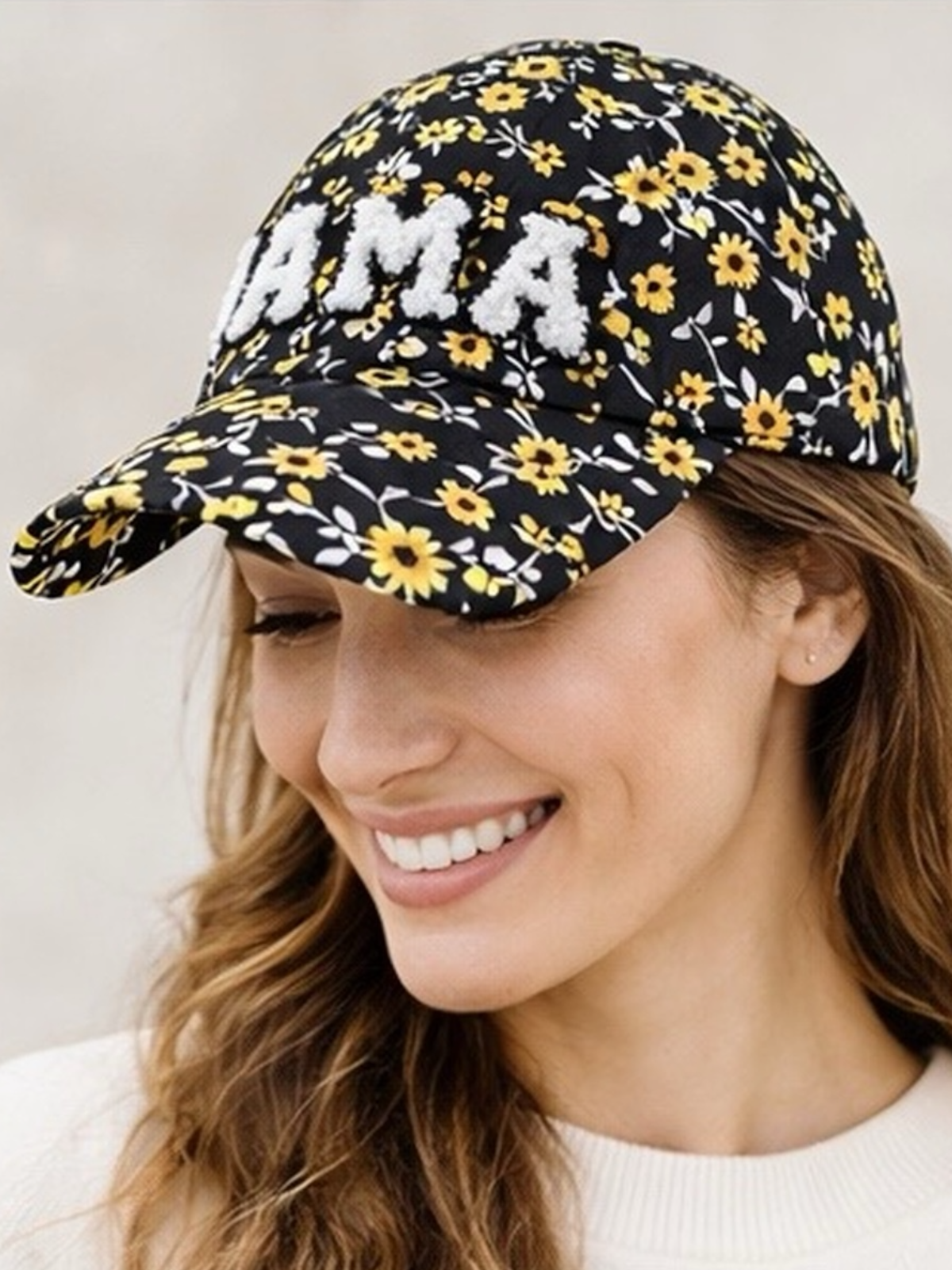 Woman smiling while wearing a black floral cap with "MAMA" in white, showcasing a cheerful expression.