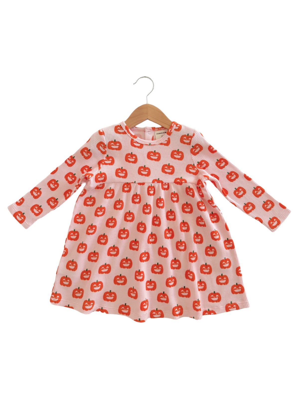 Children's dress with long sleeves featuring a playful pumpkin pattern on a light orange background.