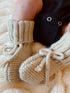 Cozy knitted baby booties with ties, resting on a soft blanket, with a child's leg partially visible.