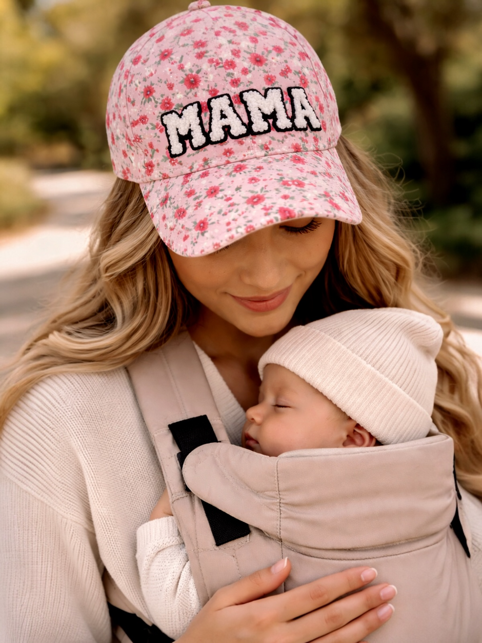 Mother in a floral cap holds a sleeping baby in a carrier, surrounded by a serene outdoor setting.