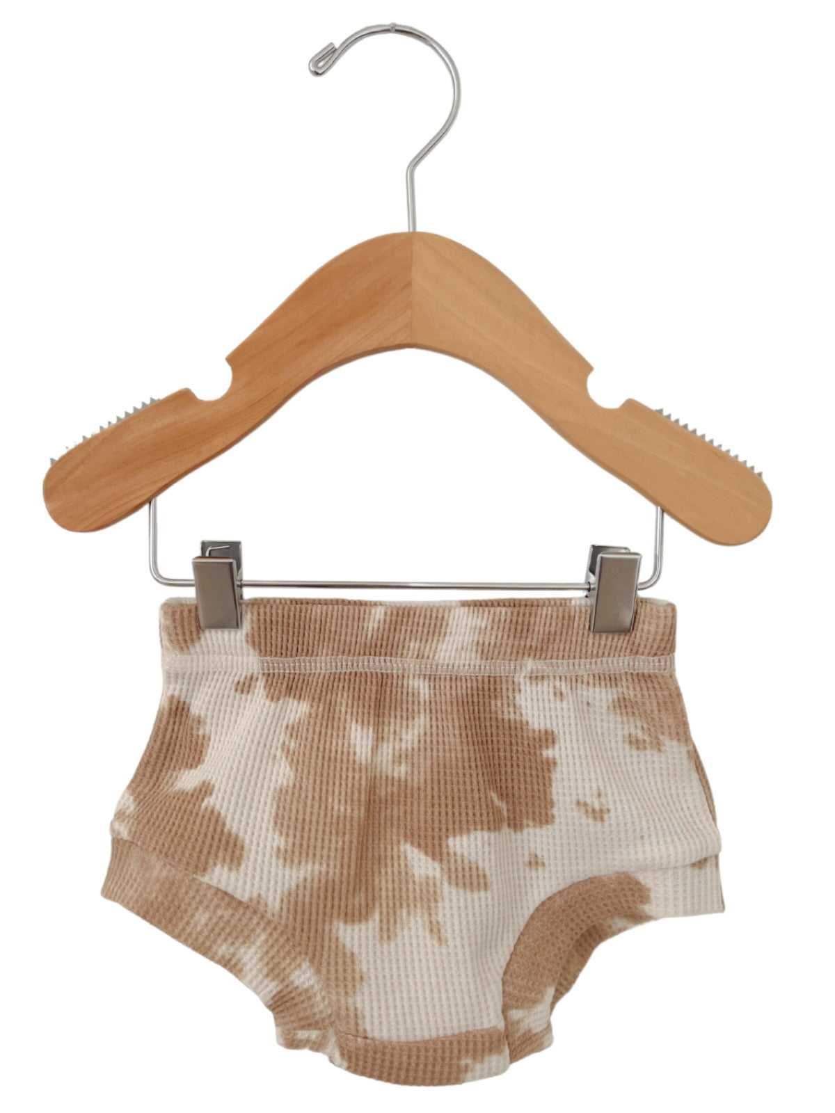 Tan tie-dye shorts hanging on a wooden hanger against a white background.