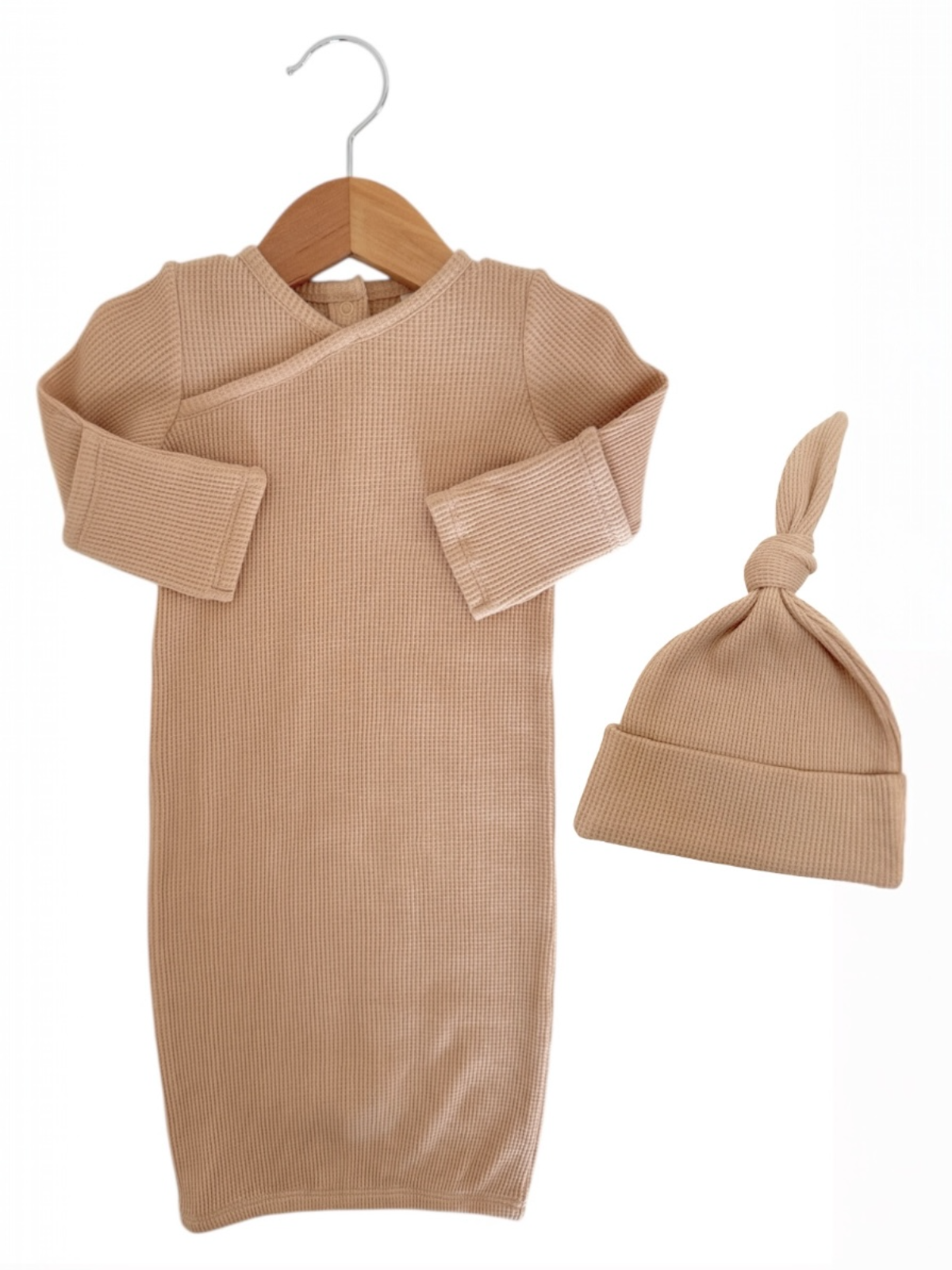 Beige baby outfit with long sleeves and a matching knotted hat, hanging on a wooden hanger.