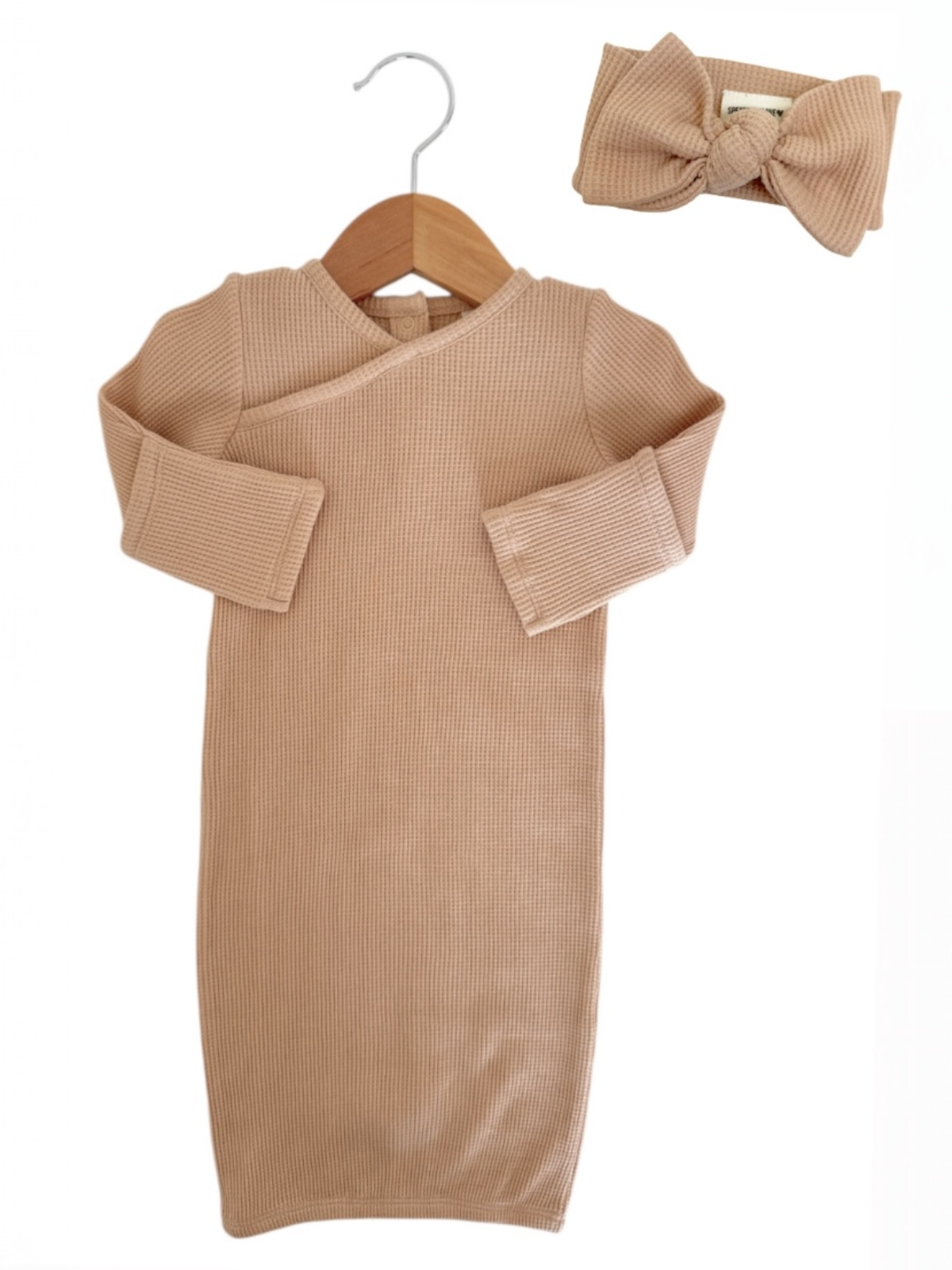 Beige baby dress with long sleeves on a hanger, paired with a matching bow headband.