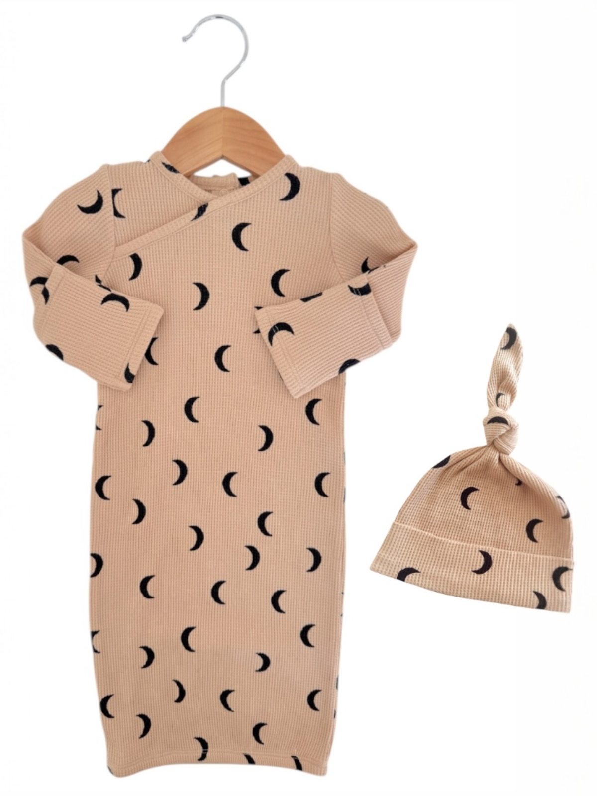 Beige baby dress with black crescent moon pattern, hanging with matching knotted hat. Ideal for newborn outfits.