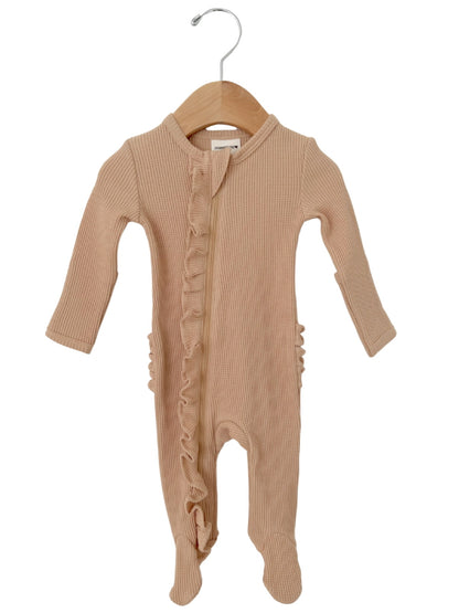 Light beige baby onesie with ruffle detailing, featuring long sleeves and footed legs, displayed on a wooden hanger.