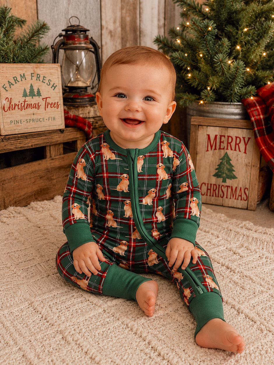 Smiling baby in festive pajamas with a dog pattern, sitting in a cozy holiday setting with Christmas decor.