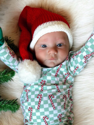 Infant wearing a festive Santa hat and candy cane-patterned outfit, lying on a plush white blanket.