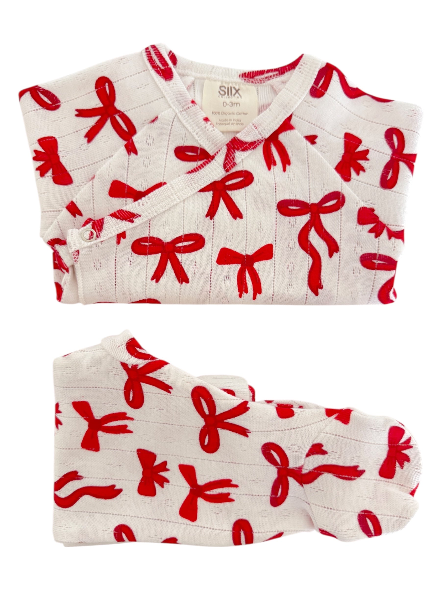 White infant outfit with red bow patterns, including a top and matching footie, made from 100% organic cotton.