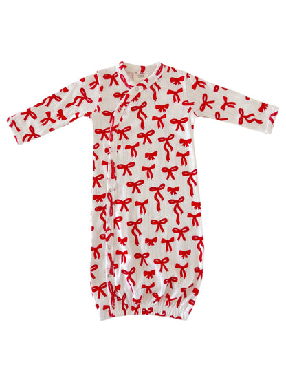 White baby gown with red bow print, featuring long sleeves and snap closures at the front.