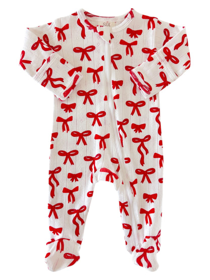 White baby onesie with red bow pattern and long sleeves, featuring snap buttons down the front.