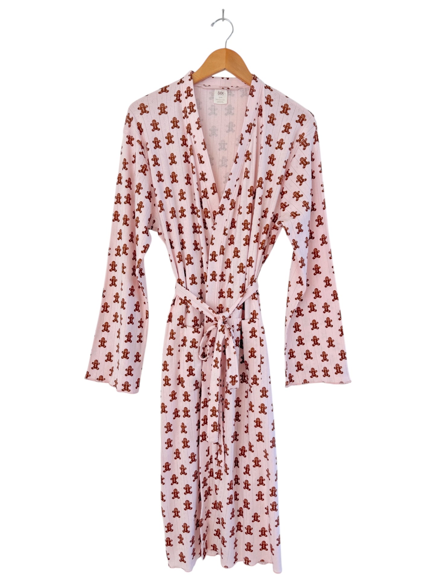 Pink robe with gingerbread man print, featuring long sleeves and a tie belt, hanging on a wooden hanger.