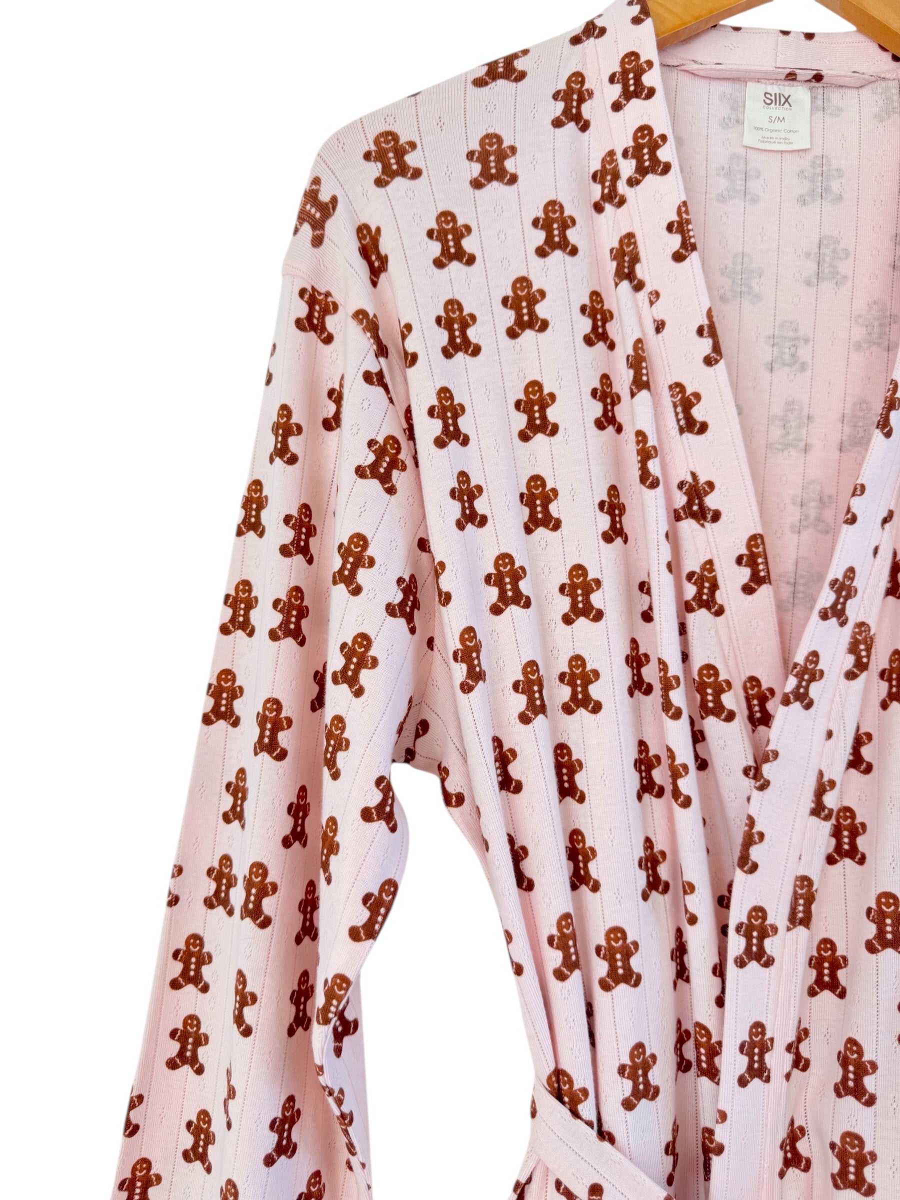 Pink robe with gingerbread man pattern hanging on hanger. Soft fabric and casual style.