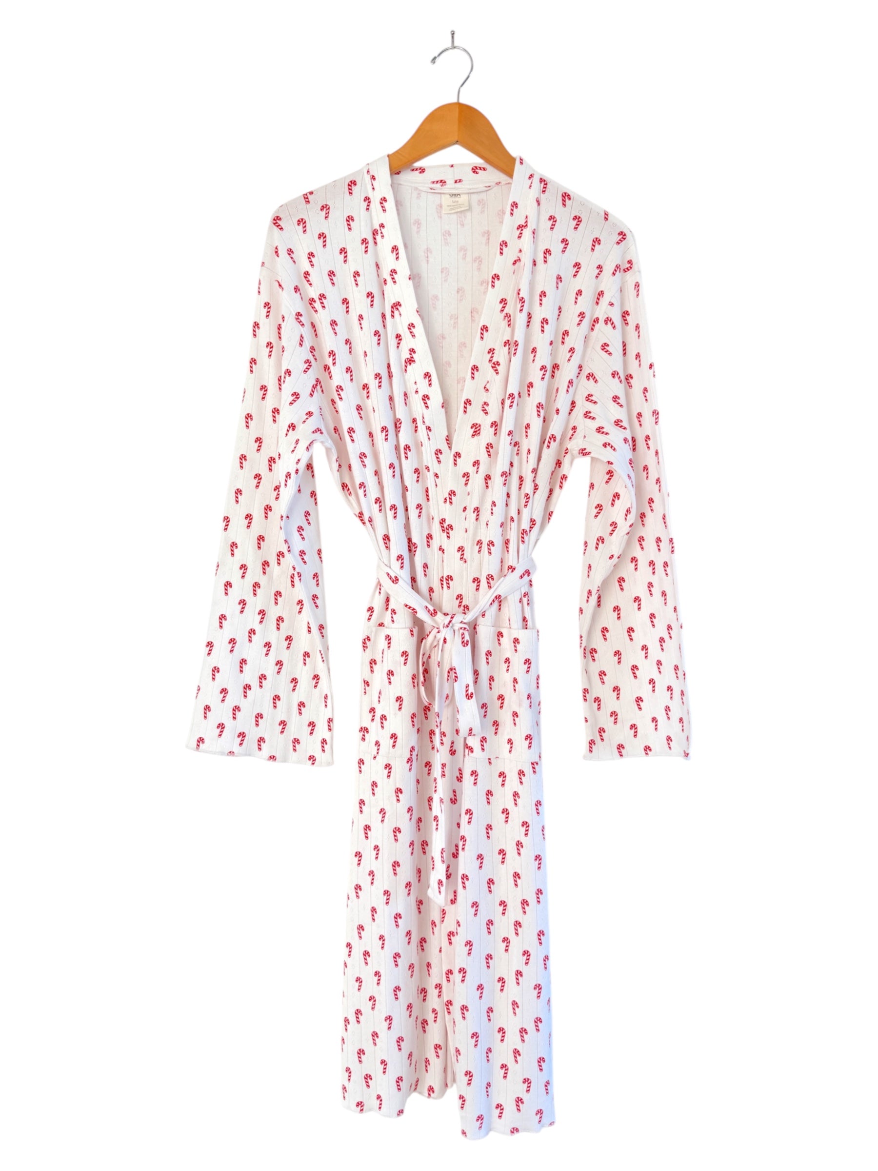 White robe with red candy cane print, displayed on a wooden hanger, featuring long sleeves and a tie waist.