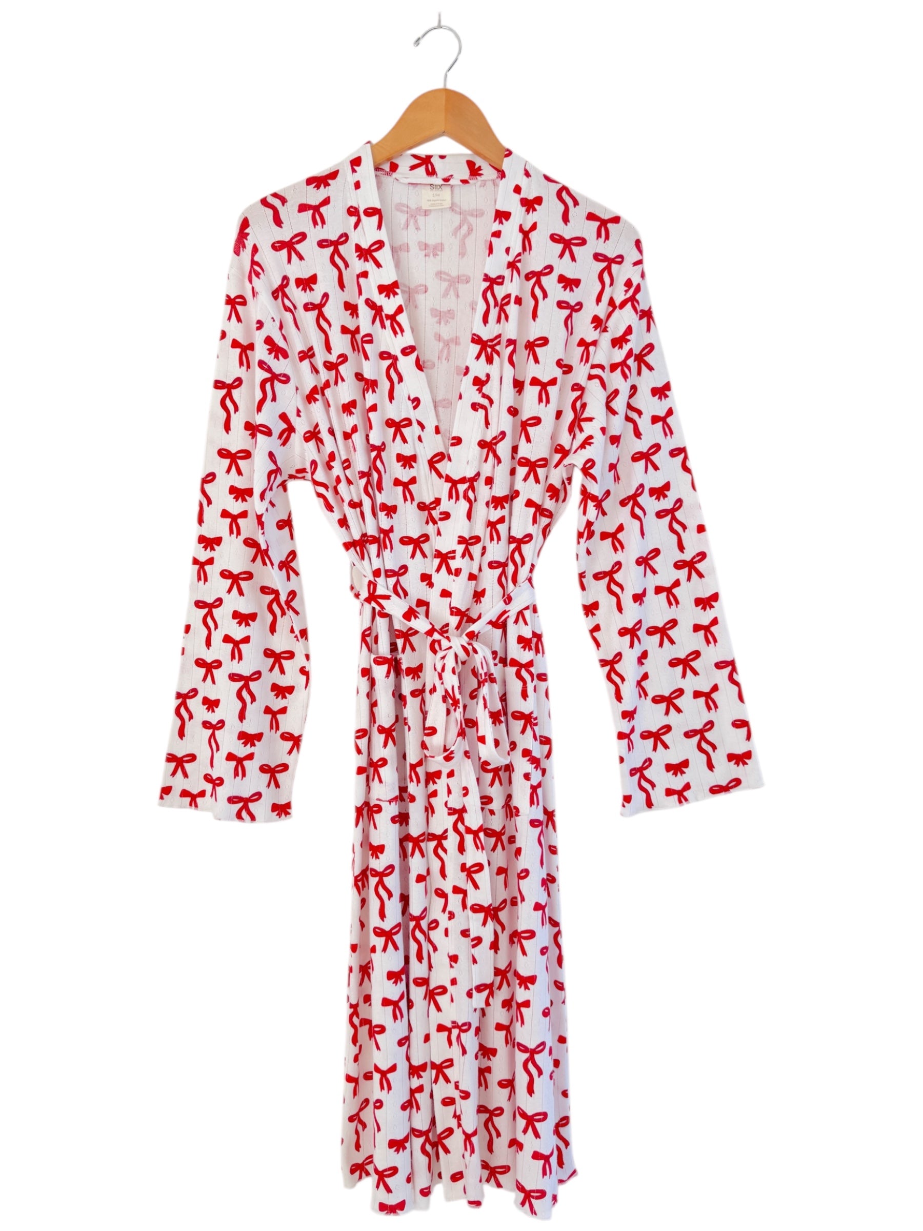 White robe featuring a playful red bow print, hung on a wooden hanger.