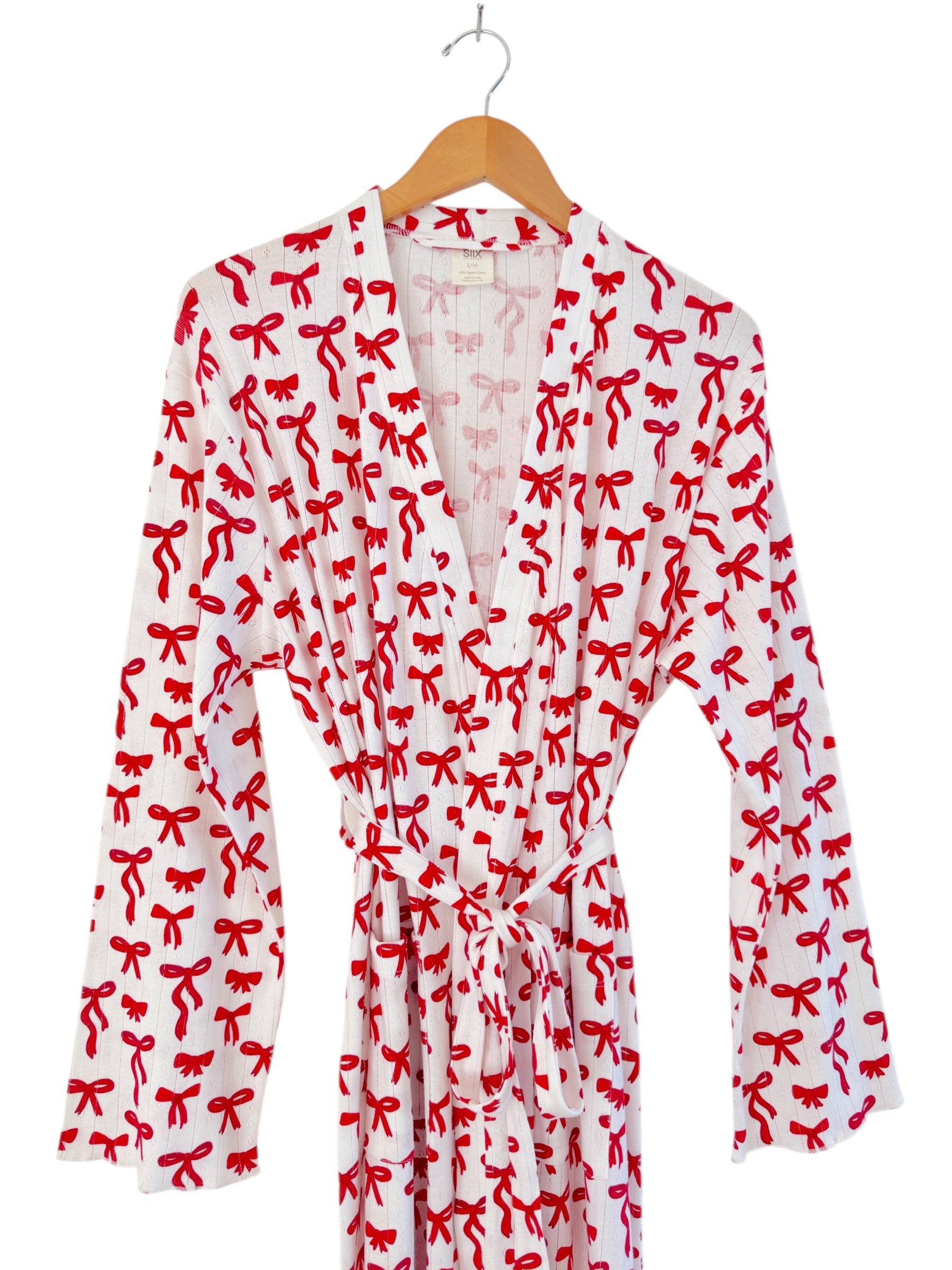 White robe with red ribbon patterns, featuring long sleeves and a tie belt. Hanging on a wooden hanger.