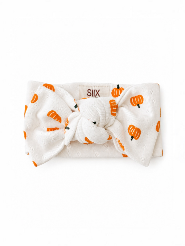 White headband with orange pumpkin print and a knot at the center, brand label visible on the back.