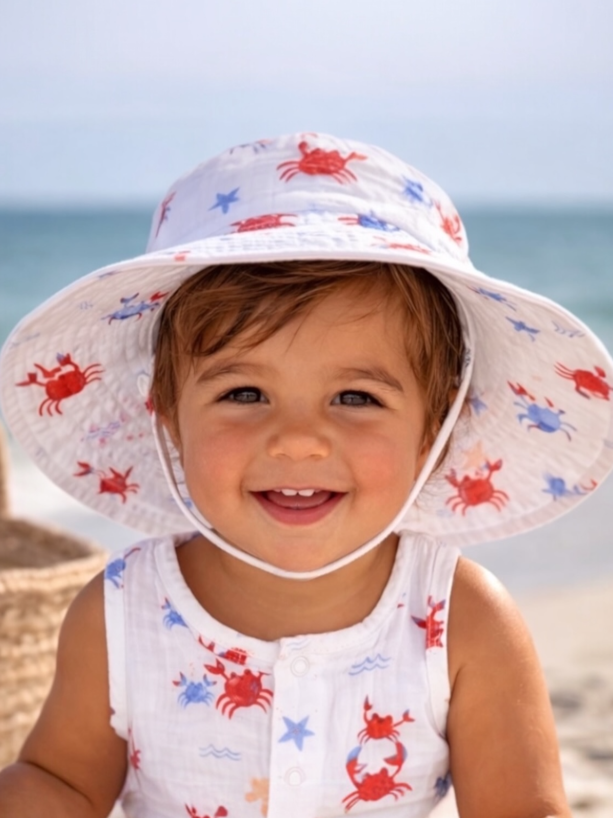 Smiling toddler in a beach hat with crabs, enjoying a sunny day at the beach.