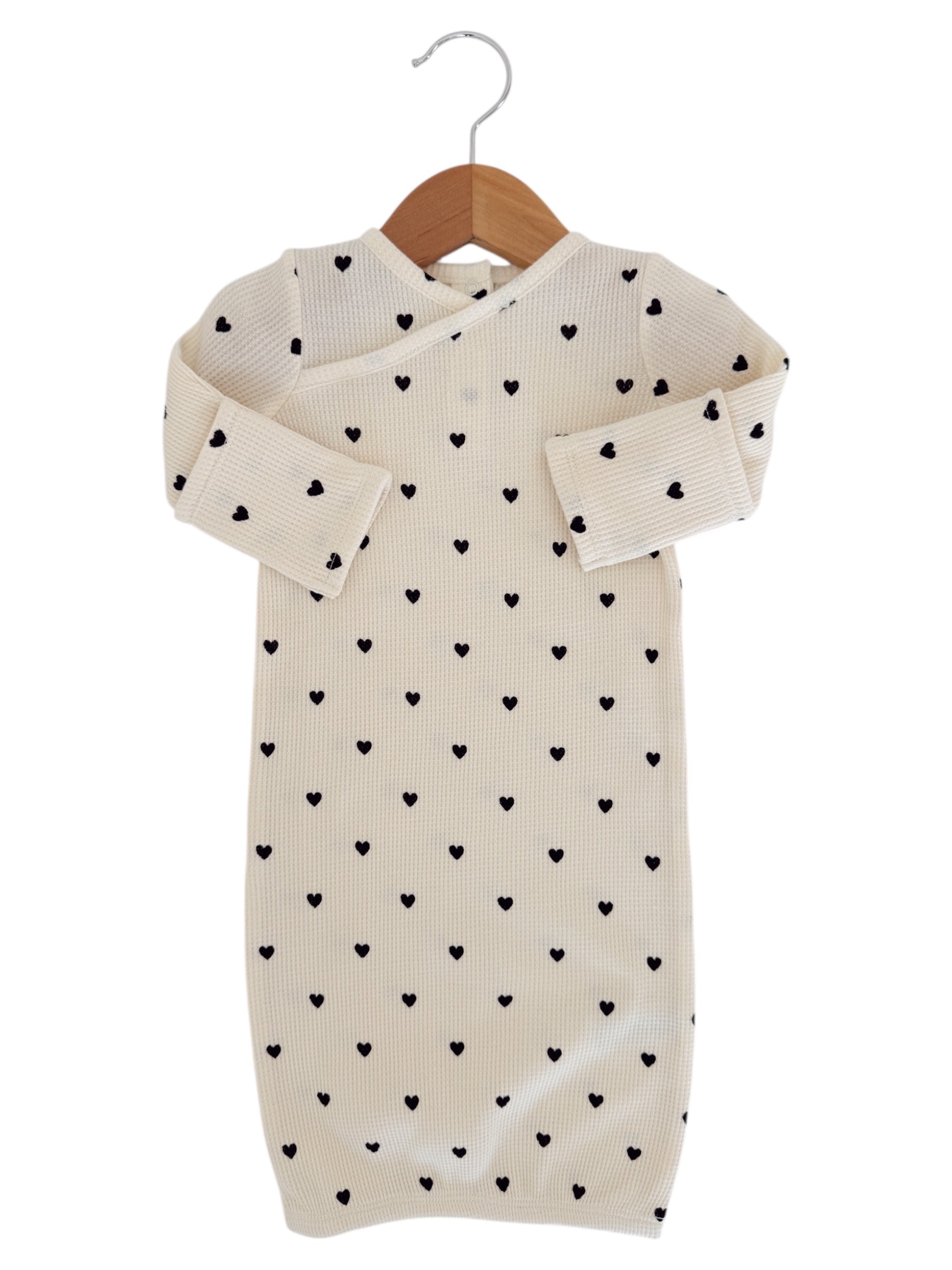 Cream-colored baby gown with black heart patterns, hung on a wooden hanger.