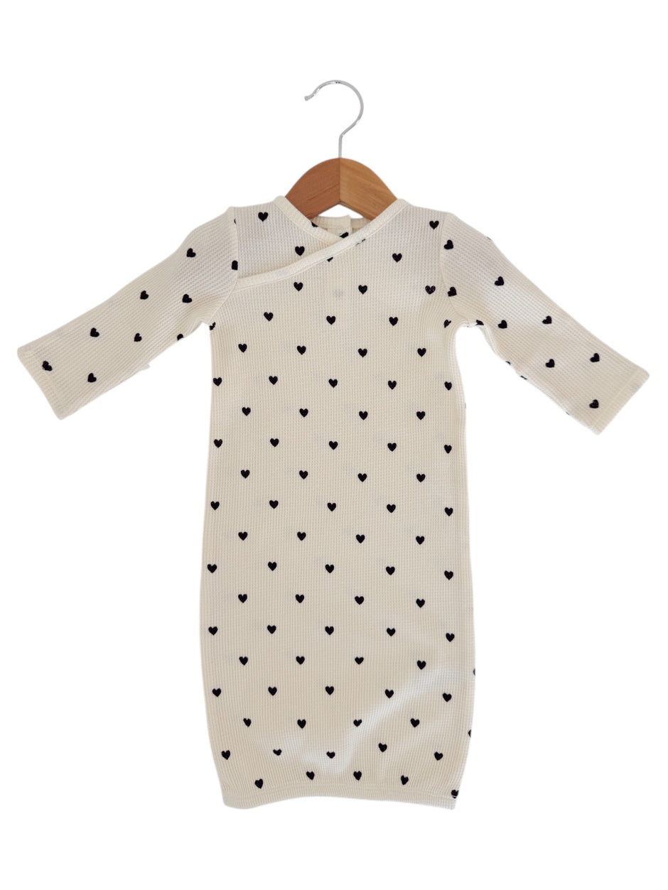Cream dress with long sleeves and black heart patterns, hanging on a wooden hanger.