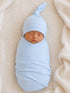 Newborn baby wrapped in light blue fabric, wearing a matching hat, resting on a textured cream blanket.