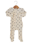 Cream baby onesie with black heart prints and ruffled detailing, hung on a wooden hanger.