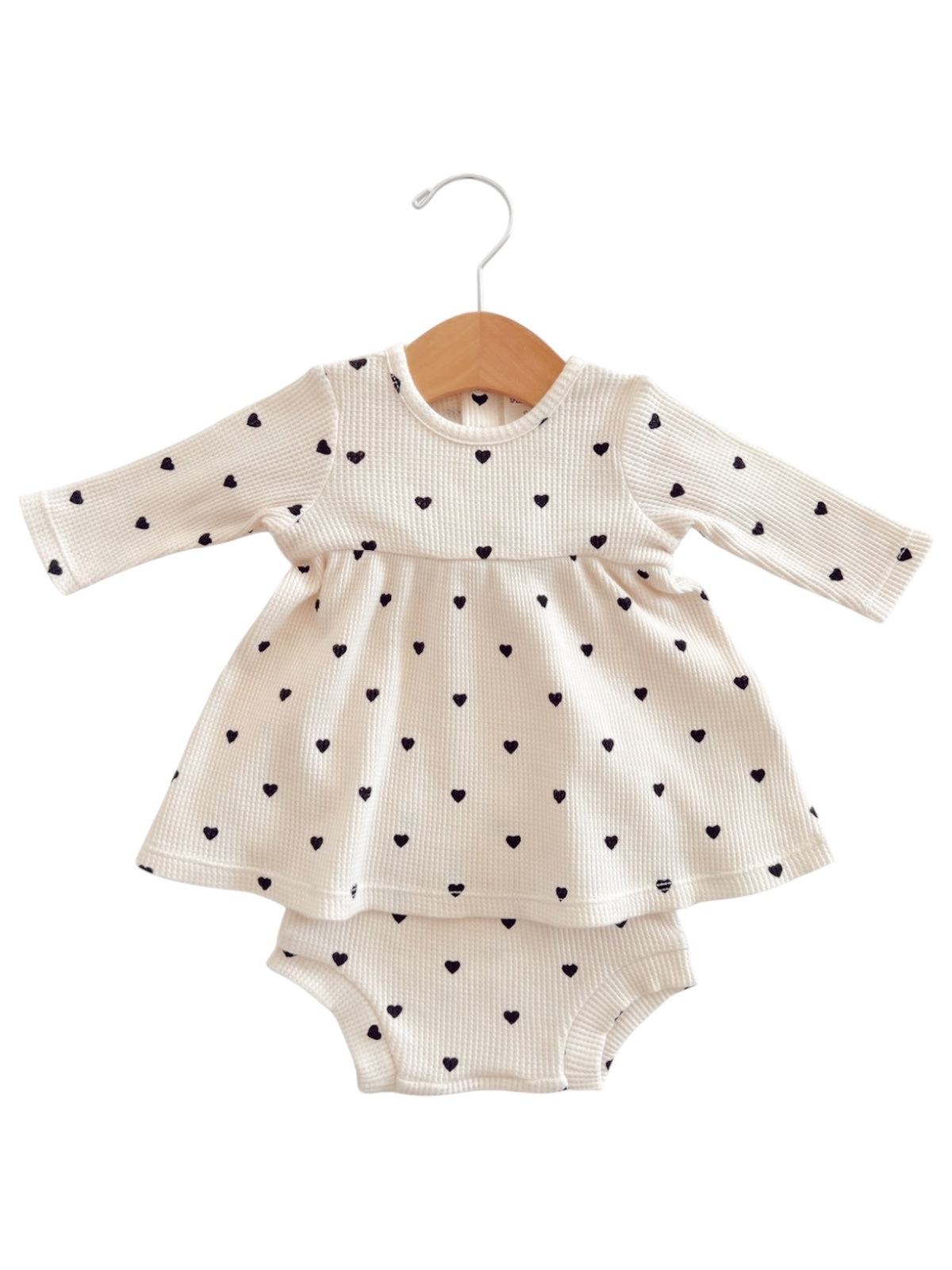 Cream dress with black heart patterns and matching romper underneath, hung on a wooden hanger.