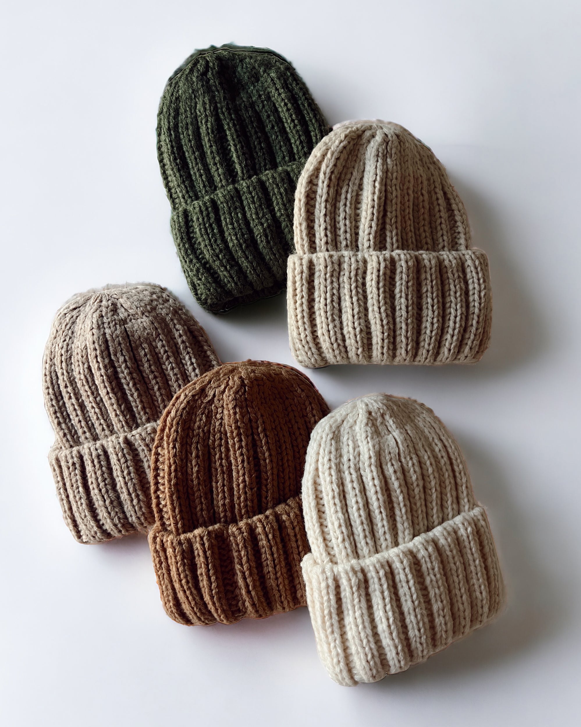 Six knitted beanies in green, beige, brown, and cream, arranged on a light background.