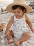 Toddler in a straw hat playing in sand, wearing a colorful fish-patterned outfit at the beach.