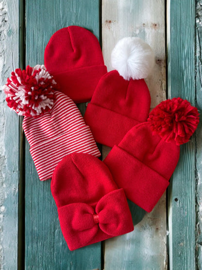 Collection of red hats with various styles, including pom-poms and bows, arranged on rustic wooden background.