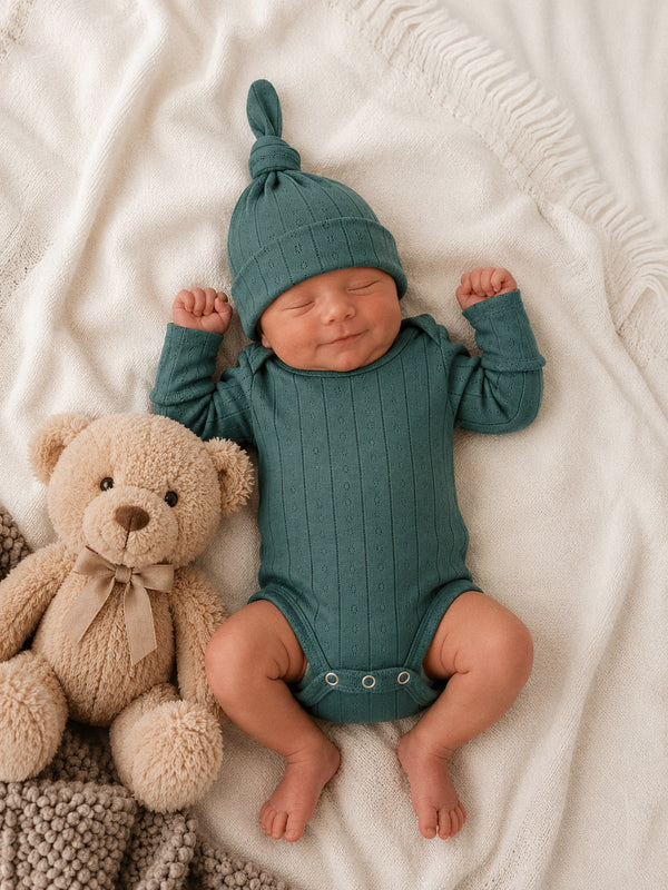Newborn in a teal outfit sleeps peacefully beside a soft teddy bear on a cozy blanket.