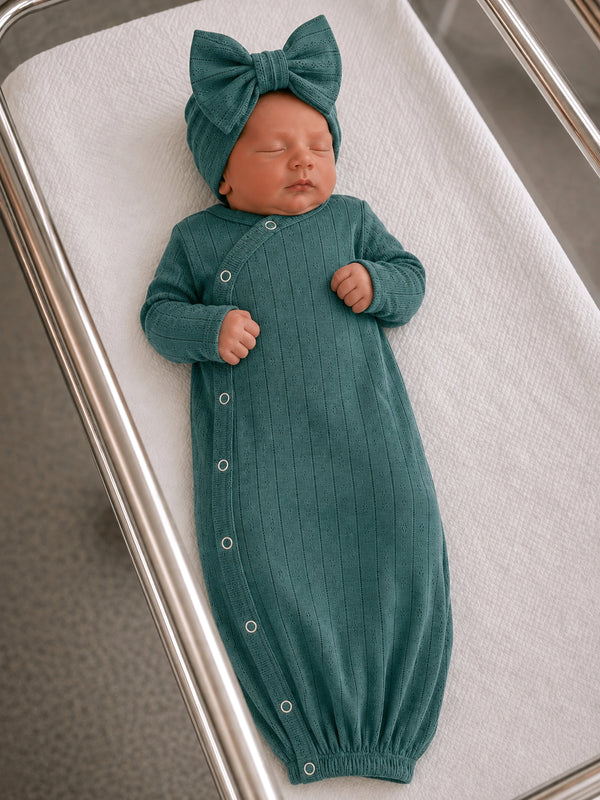 Newborn baby peacefully sleeping in a teal gown and matching bow hat on a hospital bassinet.