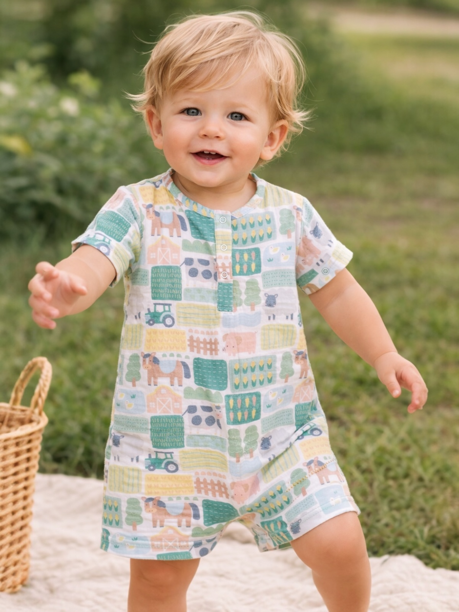 Smiling toddler in playful patterned outfit, standing on grass with a basket nearby.