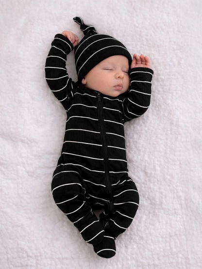 Sleeping baby in black and white striped outfit and hat on soft white blanket.