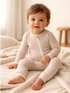 Smiling child in striped pajamas sitting on a soft blanket with a neutral background.