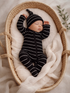 Sleeping baby in striped onesie and hat, nestled in a woven basket with soft blankets.