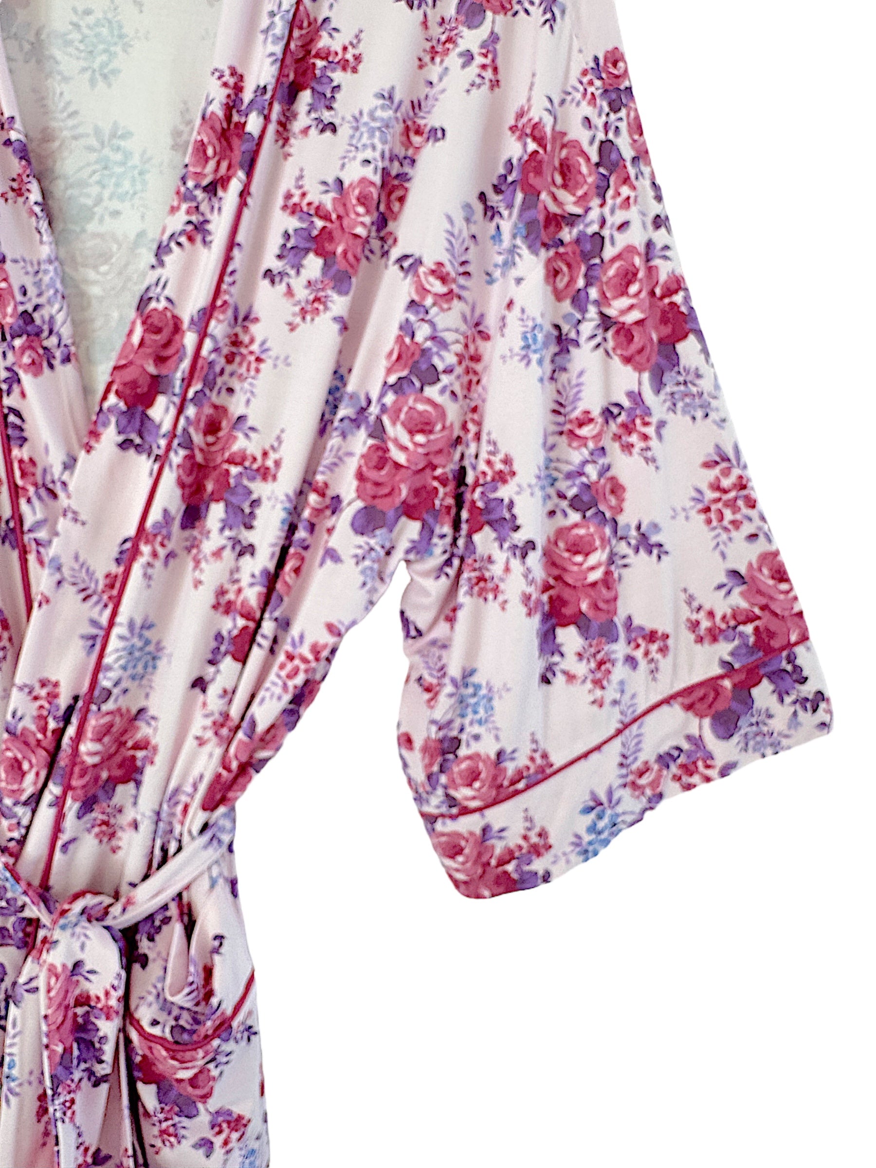 Floral-patterned robe in soft fabric, featuring pink, purple, and white hues, with a tie closure and flowing sleeves.
