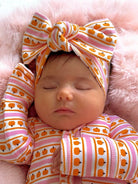 Infant girl asleep with a patterned headband and pajamas on a soft pink blanket.