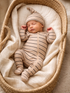 Sleeping newborn in a beige striped outfit resting peacefully in a woven basket on soft fabric.