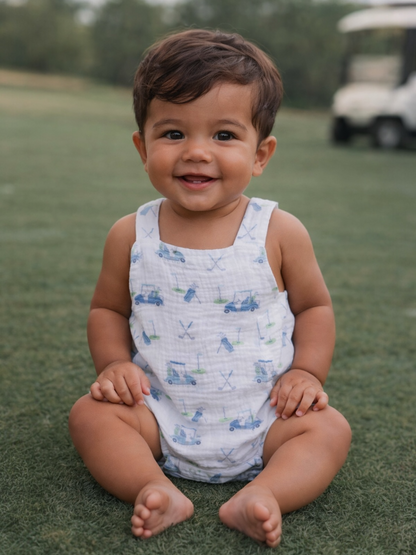 Smiling toddler in a playful outfit, sitting on grass with a golf cart seen in the background.