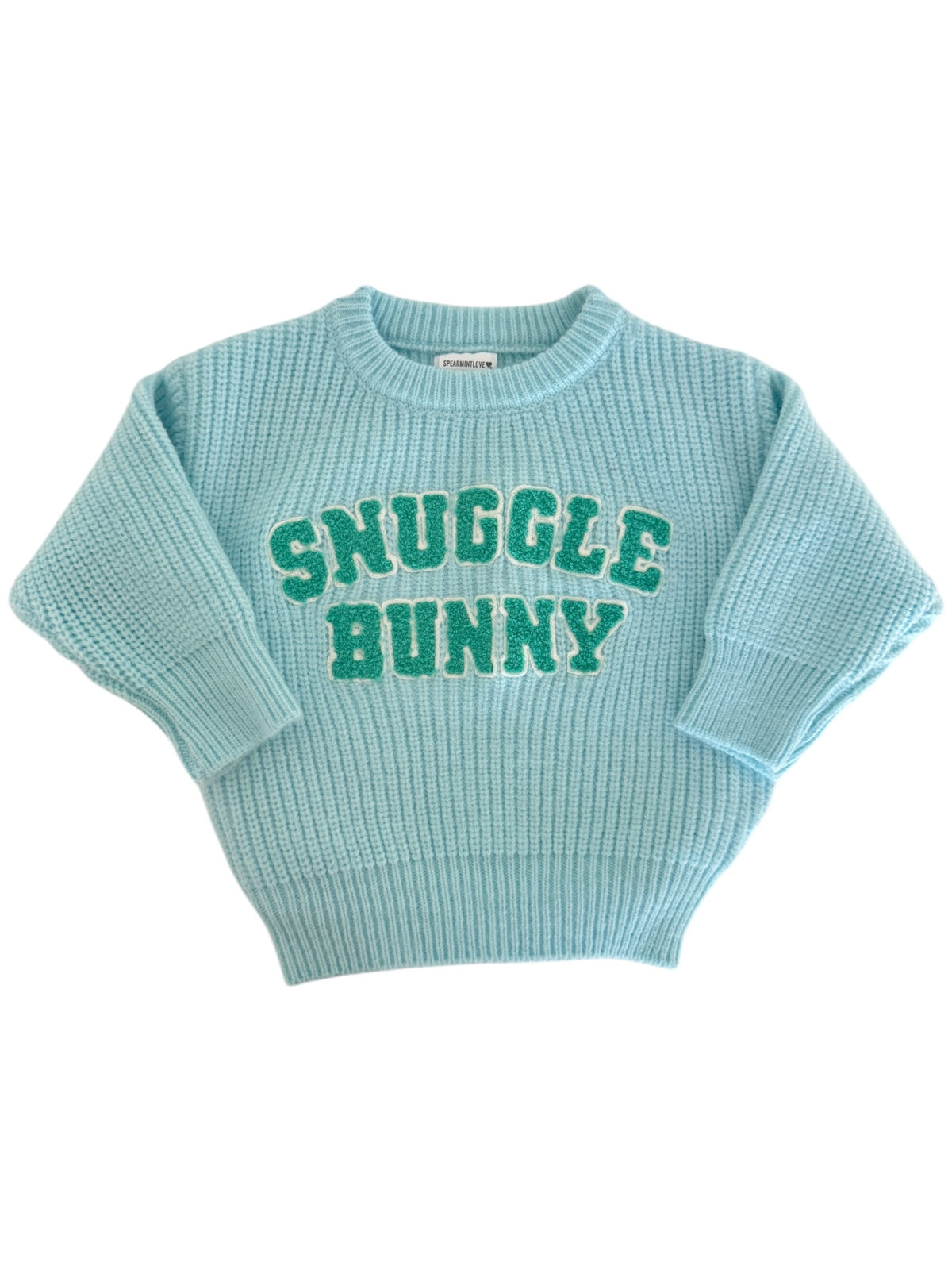 Light blue sweater with "Snuggle Bunny" text in green, featuring a knitted texture and relaxed fit.