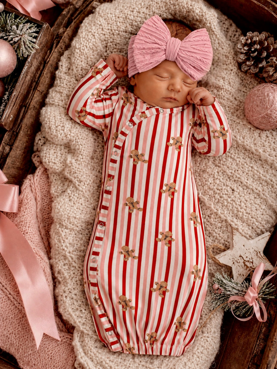 Newborn in red and white striped outfit with gingerbread prints, wearing a pink bow, resting on a cozy blanket.