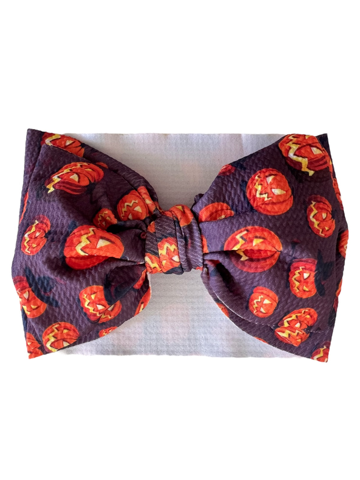 Purple hair bow with orange jack-o'-lanterns and bats, perfect for Halloween festivities.