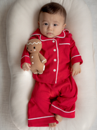 Infant in red pajamas holding a gingerbread doll, lying on a soft pillow.